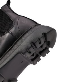 Bota deportiva negra con parte superior de cuero liso y paneles de malla, suela de goma texturizada y patrones de dibujo prominentes para un buen agarre.
