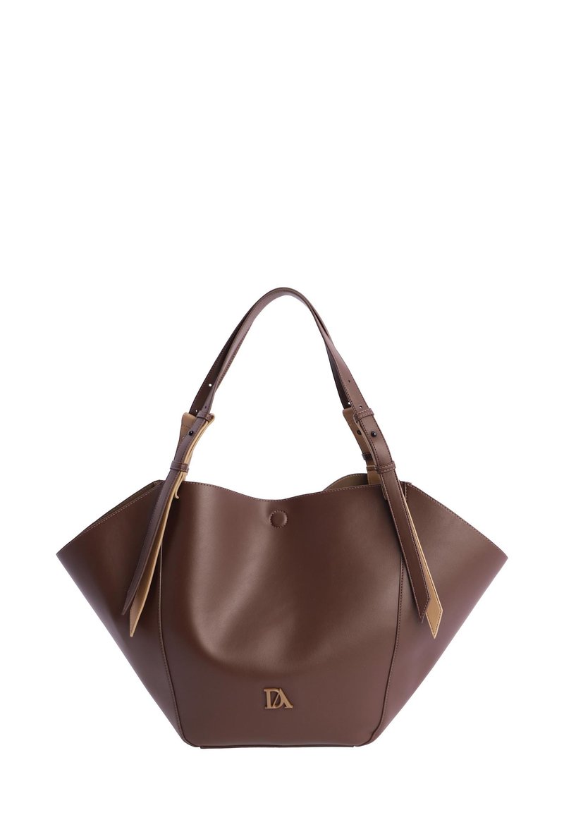 Bolso de piel marrón con forma trapezoidal amplia, doble asa superior con hebillas y pequeño emblema dorado en el centro frontal.