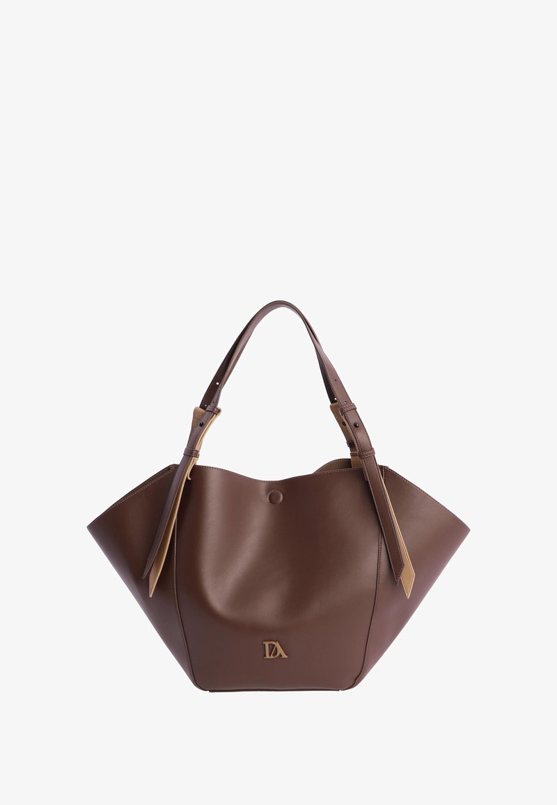 Bolso de piel marrón con forma trapezoidal amplia, doble asa superior con hebillas y pequeño emblema dorado en el centro frontal.