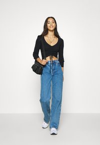 Black cropped long-sleeve top with a v-neck and drawstring detail paired with high-waisted blue wide-leg jeans and white sneakers.