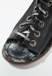 Black leather sandal with silver metallic laces and toe opening, showing worn texture on sole and upper material.