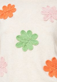 Πλεχτό πουλόβερ σε κρεμ απόχρωση με τρισδιάστατα εφαρμοστά λουλούδια σε ροζ, πράσινο και πορτοκαλί, με μαλακή υφή και στρογγυλή λαιμόκοψη.