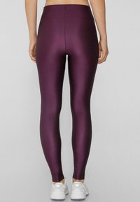 Leggings viola a vita alta realizzati in un tessuto morbido e elasticizzato, con una silhouette aderente e scarpe da ginnastica bianche a contrasto.