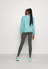 Ljusblå sweatshirt med ribbad mudd, kombinerad med mörkgrå leggings med grafisk detalj på sidan, avslutad med mintgröna sneakers.