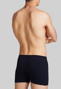 Boxer briefs neri in cotone morbido, con una vestibilità aderente e una cintura liscia, visti da dietro su uno sfondo grigio.