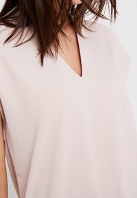 Ljust rosa topp med kort ärm och V-ringning. Mjuk textur och avslappnad passform, med minimala sömmar och inga synliga dekorationer.