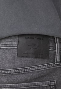 Grå denimjeans med en teksturert overflate, med et svart skinnlapp merket "JACK & JONES" på baklivet.