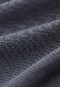Detailopname van donkergrijs gebreide stof met een fijne, geribde textuur en zachte plooien die een subtiele schaduw creëren.