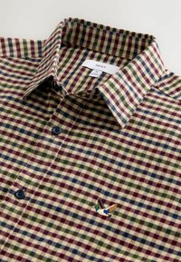 Karierte Hemd mit grünen, blauen und burgunderfarbenen Quadraten, dunklen Knöpfen und einer gestickten fliegenden Wildente nahe der unteren rechten Ecke des Kragens.