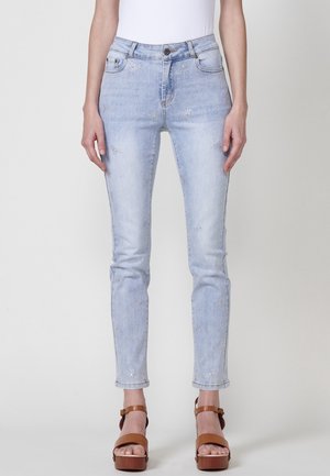 Lichtblauwe skinny jeans met subtiele sterversieringen, gedragen met bruine platformsandalen en een witte ingestopte top.