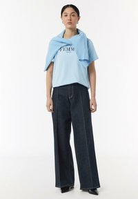 Hellblaue Kurzarm-T-Shirt mit dem Aufdruck "FEMME", kombiniert mit dunkelblauen weit geschnittenen Jeanshosen mit orangenen Nähten.