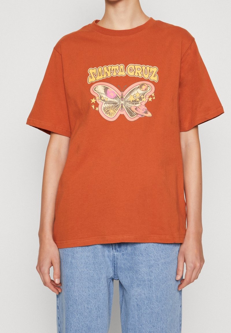 Rost-orange bomullströja med en grafisk fjärilsdesign i rosa och gult, med stjärnor och texten "ANTA CRUZ" i en retrostil.