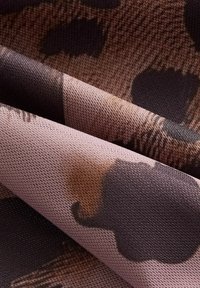 Tissu textile à surface texturée, présentant un motif abstrait rose et marron ressemblant à des taches animales. Plusieurs couches sont visibles.