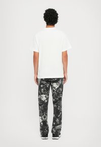 Balti trumpu rankoviu marškiniai, derinami su juodomis raštuotomis kelnėmis, turinčiomis spiralės ir dizaino motyvus, o derinį užbaigia balti batai.