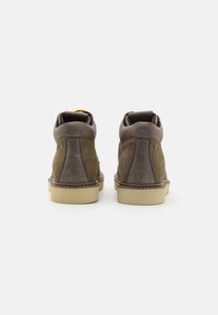 Zapatos altos de cuero marrón con un acabado de ante suave, costuras en contraste y una suela de goma ligera. Incluyen un collar en el tobillo y una lengüeta en la parte posterior.
