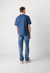 Blå bomulds T-shirt med korte ærmer og rund halsudskæring, parret med lyseblå denim jeans. Har minimal branding på ryggen.
