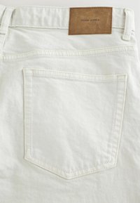 Valged denim püksid pruuni nahast tagakotiga, millel on silt "DENIM SUPPLY." Üks tagakott ja nähtavad õmbluse üksikasjad.