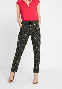 Zwarte broek met een abstracte tan- en roomkleurige print, voorzien van een elastische tailleband met een trekkoord, gestyled met een rode colshirt.
