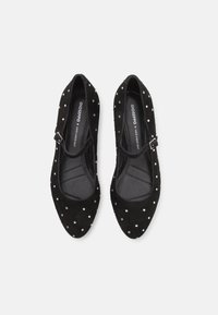 Svarta mockaskor med spetsig tå, utrustade med ett rem med en silverfärgad spänne och dekorerade med små silverfärgade nitar över ytan.