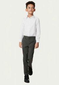 Witte blouse met lange mouwen, grijze broek en zwarte schoenen. De blouse heeft een klassieke kraag; de broek is op maat gemaakt met een gladde textuur.