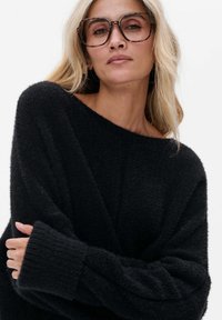 Zwarte, textuurrijke oversized trui met een brede off-shoulder halslijn en lange mouwen. De stijl heeft ribgebreide manchetten en een zachte brei-afwerking.