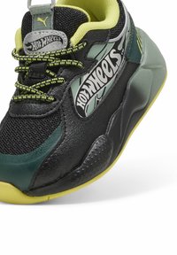 Pantofii sport negri și verzi au o parte superioară din plasă, accente din piele texturată și o talpă din cauciuc galben, având brandingul 'Hot Wheels' pe lateral.