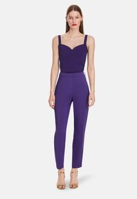 Purple fitted top with thick straps and a sweetheart neckline paired with matching tailored purple trousers and gold ankle-strap heels.