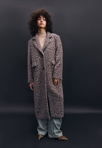 Leopardenmuster langer Mantel aus weichem, strukturiertem Stoff, mit eingeschnittenem Kragen, vorderen Knöpfen und zwei Seitentaschen. Über lässigen Jeans getragen.