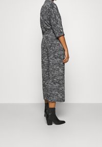 Svart och vit mönstrad jumpsuit med lös passform, korta ärmar och samlad midja, ihop med svarta klackstövlar som går upp till anklarna.