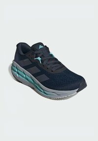 Chaussure de sport noire avec accents turquoise, empeigne en mesh, langue texturée, design trois bandes Adidas bien en évidence et semelle amortie.