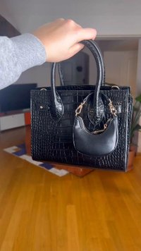 Musta krokotiilin kuvioitu nahkainen käsilaukku, jossa on kaksi yläkahvaa ja pieni irrotettava musta pussukka, joka on kiinnitetty kultaisella ketjulla.