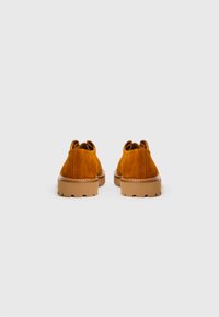 Chaussures en daim jaune-brun avec une forme arrondie. Semelles en caoutchouc texturé tan épaisses et accents cousus au niveau du talon. Design minimaliste.