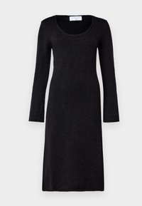 Robe longue en maille noire à manches longues, col rond, taille cintrée et ourlet au niveau des genoux, présentée sur un fond gris clair uni.