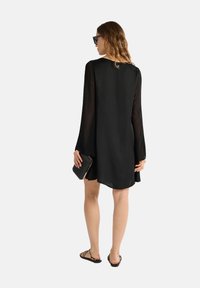 Abito nero con maniche lunghe e trasparenti, dal taglio morbido, con scollo rotondo e un tessuto текстurato. Abbinato a sandali neri e a una pochette.