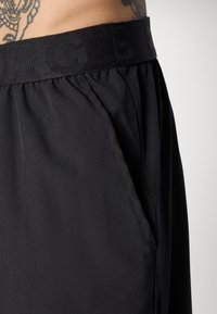 Μαύρο σορτσάκι με ελαστική μέση, από ελαφρύ και λείο ύφασμα, με πλαϊνές τσέπες και διακριτική ραφή.