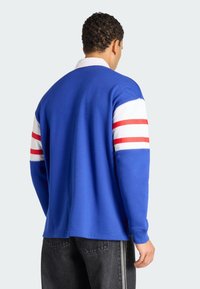 Camicia a maniche lunghe blu con accenti a strisce bianche e rosse sulle maniche. Presenta un colletto e una texture del tessuto liscia. Design casual.