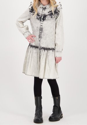 Un vestito bianco a maniche lunghe con effetto acid-wash nero, colletto a volant e vita arricciata, abbinato a stivaletti neri alla caviglia e leggings.