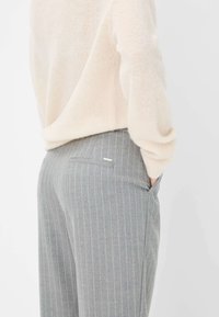 Grijze pinstripe broek met een gestructureerde afwerking, voorzien van zijzakken en een subtiele merkaanduiding op de achterkant. Gepaarde met een lichte trui.