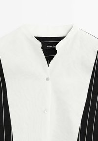 Svart- och vitrandig skjorta med V-ringning, med knappstängning och ett lätt material. Etiketten säger "Massimo Dutti."
