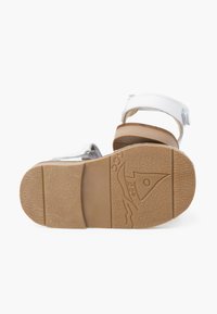 Sandale marron clair avec une semelle en caoutchouc durable, des sangles blanches réglables et un fini texturé. Détail de logo notable sur la semelle.