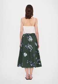 Fustă midi verde cu un model floral, prevăzută cu un brâu elastic, asortată cu un top alb fără mâneci, cu bretele subțiri.