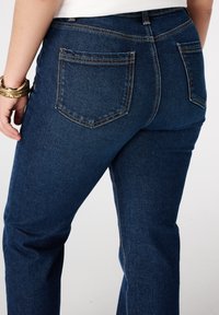 Donkerblauwe spijkerbroek met een hoge taille, voorzien van twee achterzakken en contrasterende stiksels, een gladde textuur en een rechte pijpontwerp.