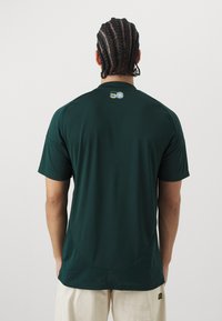 Groene sportshirt met een ronde hals, korte mouwen en een gladde textuur. Bevat een klein logo op de bovenrug, zonder zichtbare patronen.