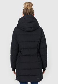 Sort pufferjakke med stor hætte, kviltet design, sidesnore detaljer og ribbede manchetter. Længden strækker sig til midten af låret.