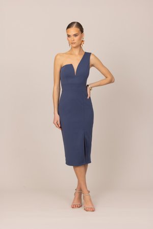 Kobieta ubrana w dopasowaną, granatową sukienkę na jedno ramię o długości do kolan z przednim rozcięciem, stojąca z jedną ręką na biodrze i nosząca kolczyki.