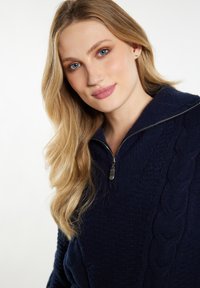 Pulover bleu marin cu guler cu fermoar, design texturat de tricotaj cu cablu și material moale. Are mâneci lungi și o croială relaxată.