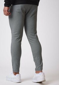 Grå atletiske bukser lavet af tekstureret stof, slim-fit design, med elastisk talje og sidesømme, parret med hvide sneakers.