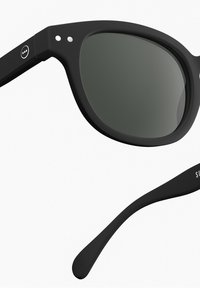 Czarne okulary przeciwsłoneczne o matowym wykończeniu, kwadratowych soczewkach i dwóch małych białych akcentach na oprawie. Na zauszniku znajduje się subtelny napis marki.