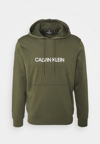 Olivengrøn hættetrøje med kængurulomme, hvid tekst med ordene "CALVIN KLEIN" og ribkant ved ærmer og kant. Glat tekstur.