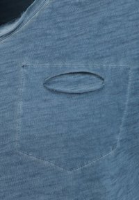 Camicia di cotone blu con scollatura rotonda e una piccola tasca sul petto con un'apertura ovale unica. Texture morbida e design casual.